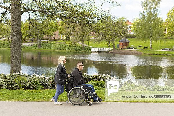 Schweden, Ostergotland, Mjolby, Mann im Rollstuhl mit persönlicher Assistentin im Park