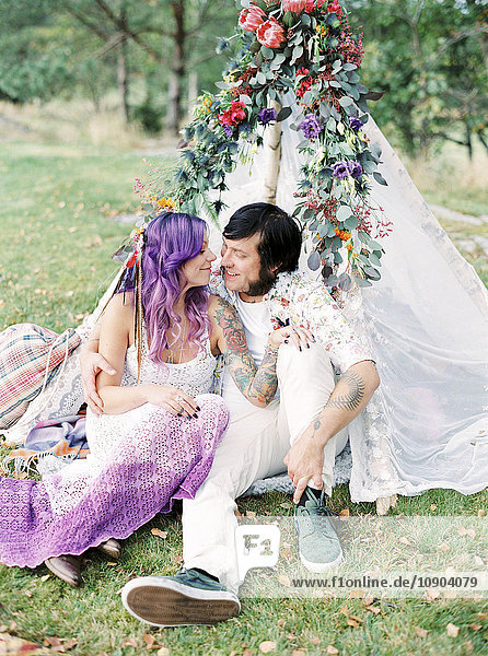 Schweden  Braut und Bräutigam sitzen auf Gras bei einer Hippie-Hochzeit im weißen Zelt