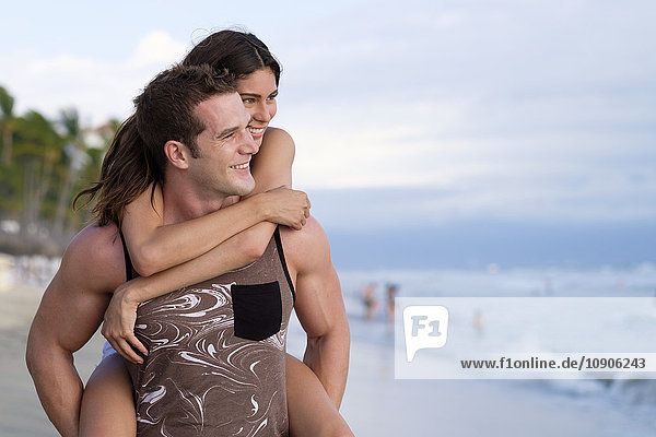 Young man giving his girlfriend a piggyback ride on the beach