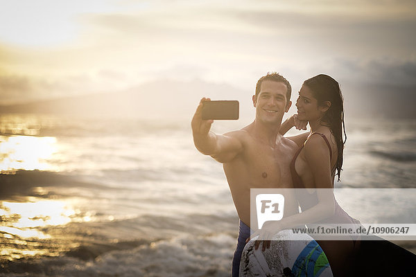 Ein junges Paar  das in der Dämmerung einen Selfie am Strand nimmt.