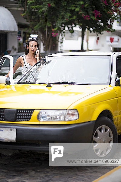 Young woman on the phone entering a taxi