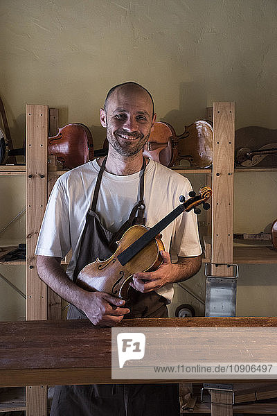 Smiling luthier holding a violin in his workshop