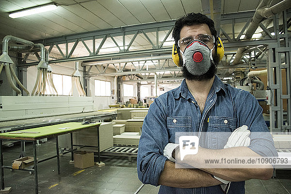 Man with hearing protection  mask  safety glasses and gloves with his arms crossed in a factory