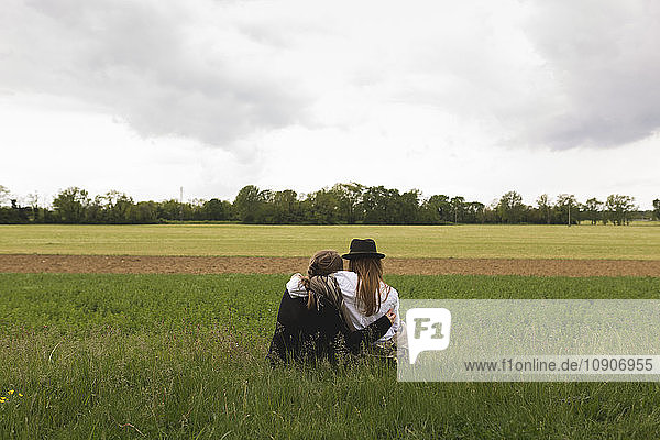 Back view of two friends sitting on a meadow at countryside