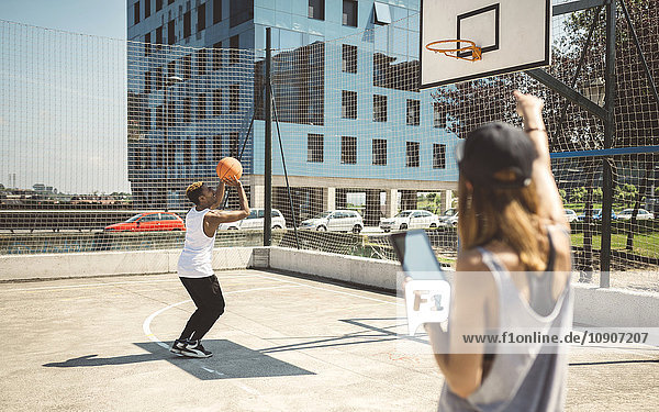 Junge Frau mit digitalem Tablett im Gespräch mit einem Basketballspieler