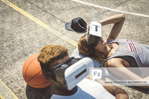 Young couple using virtual reality glasses  resting heads on basketball