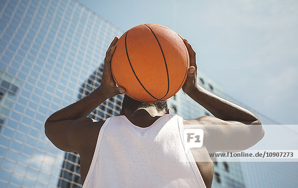 Junger Mann hält Basketball hinter dem Kopf