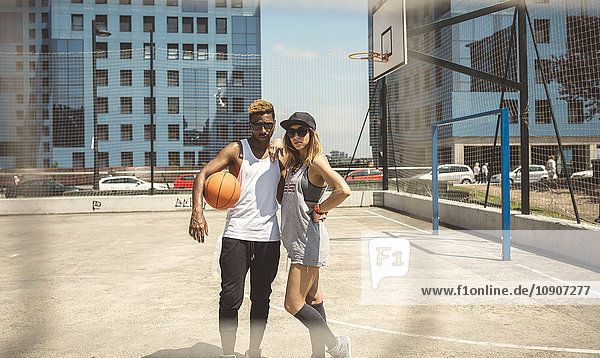 Junges Paar steht auf dem Basketballfeld und schaut in die Kamera.