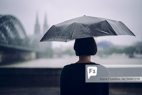 Deutschland  Köln  Rückansicht einer Frau mit Regenschirm an einem Regentag