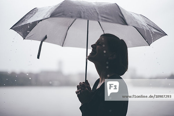 Lachende Frau mit Regenschirm an einem regnerischen Tag