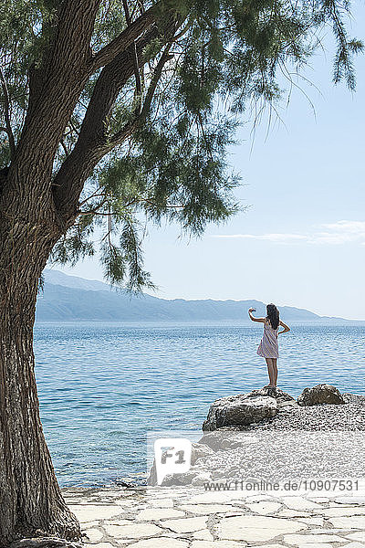 Greece  Sergoulas  woman taking pictures with smartphone at the coast