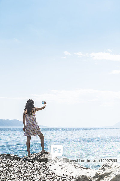 Griechenland  Sergoulas  Frau beim Fotografieren mit dem Smartphone an der Küste