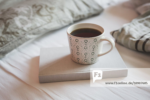 Buch und Tasse schwarzen Kaffee auf einem Bett