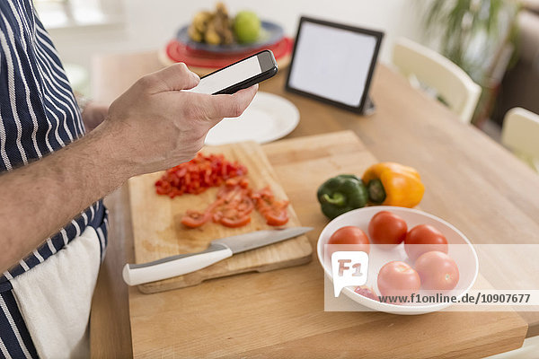 Mann mit Smartphone bei der Zubereitung von Speisen in der Küche  Nahaufnahme