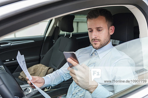 Businessman with documents and cell phone in car