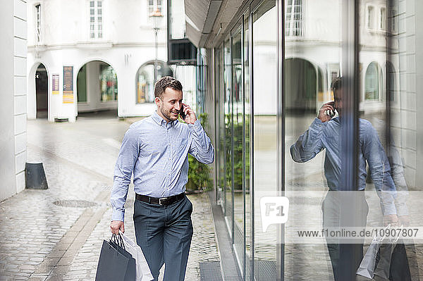 Young man with shopping bags on the phone passing a shop