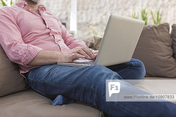 Mature man sitting on couch using laptop
