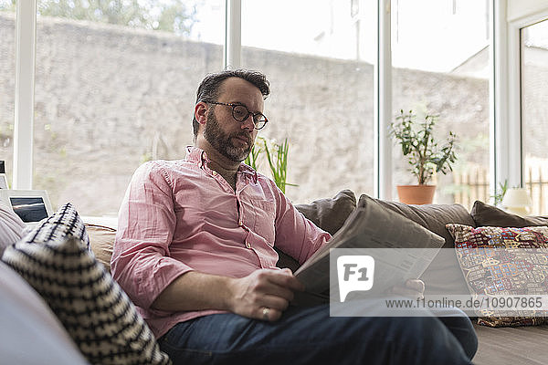 Mature man sitting on couch reading newspaper