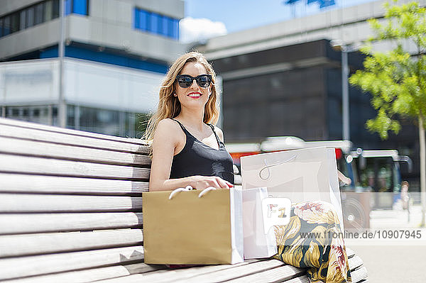 Portrait of smiling young woman sitting on a bench with shopping bags
