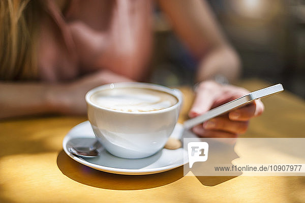 Woman sitting in a coffee shop with Cappuccino holding smartphone  close-up