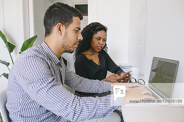 Young businessman and woman working together in office  using laptop