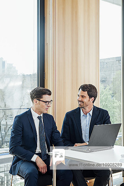 Two businessmen with laptop talking in office