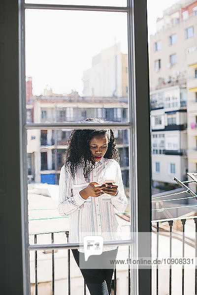 Young businesswoman standing on balcony  checking messages on smart phone