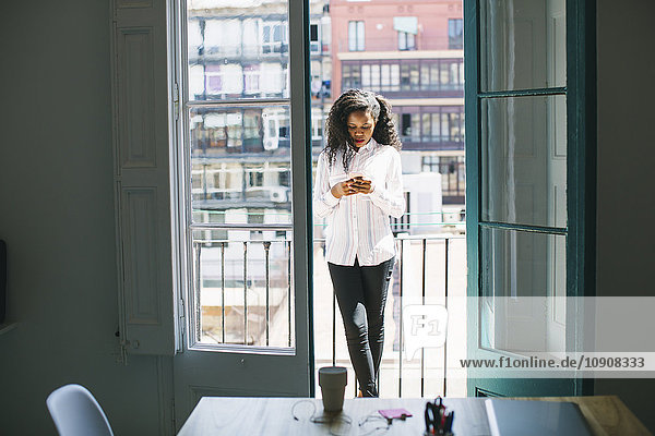 Junge Geschäftsfrau auf dem Balkon stehend  Nachrichten auf dem Smartphone abrufend