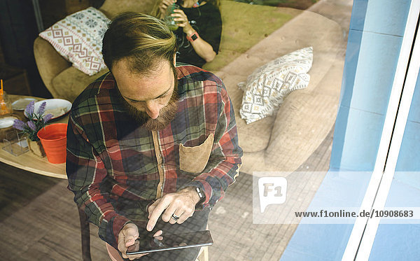 Porträt eines bärtigen Mannes mit digitalem Tablett hinten im Cafe