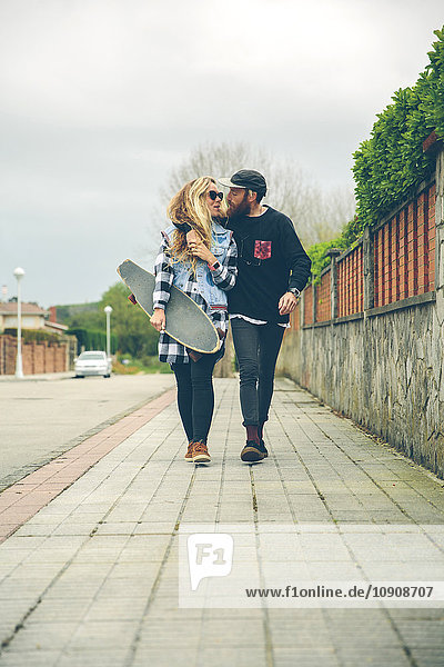 Couple in love with skateboard walking on pavement