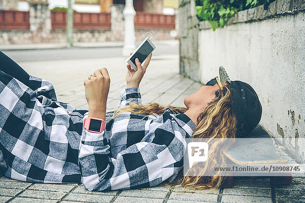 Junge Frau auf dem Skateboard liegend mit Blick auf das Handy