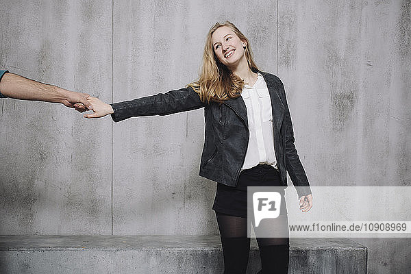 Couple in front of concrete wall  woman holding hand of man
