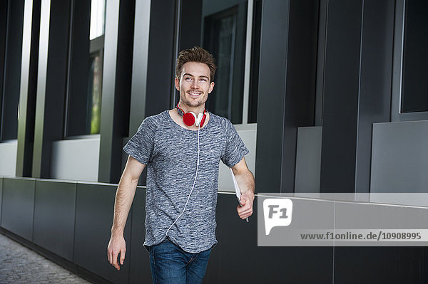 Portrait of walking young man with headphones and digital tablet