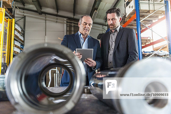 Two engineers with digital tablet in front of hydraulic cylinder