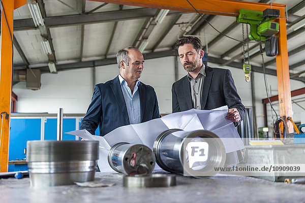 Two engineers with construction plan in front of hydraulic cylinder