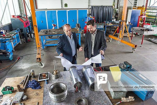 Two engineers with construction plan in front of hydraulic cylinder