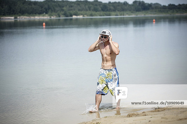 Man in trunks hearing music with headphones while wading at lakeshore