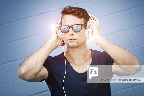 Porträt eines Mannes mit verspiegelter Sonnenbrille  der Musik über Kopfhörer hört.