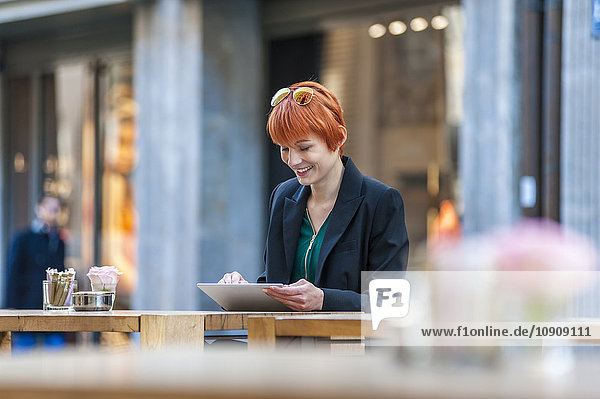 Lächelnde junge Frau mit digitalem Tablett im Outdoor-Café
