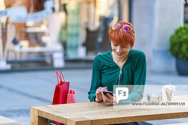 Lächelnde junge Frau mit Handy im Outdoor-Café