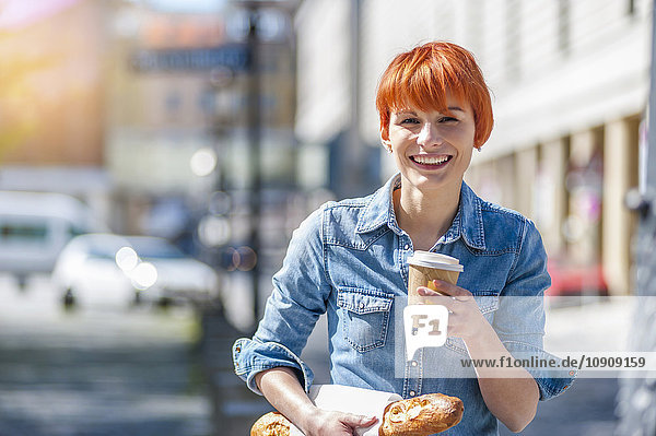 Porträt einer lächelnden jungen Frau mit Kaffee und Baguette