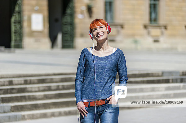 Lächelnde junge Frau beim Musikhören im Freien