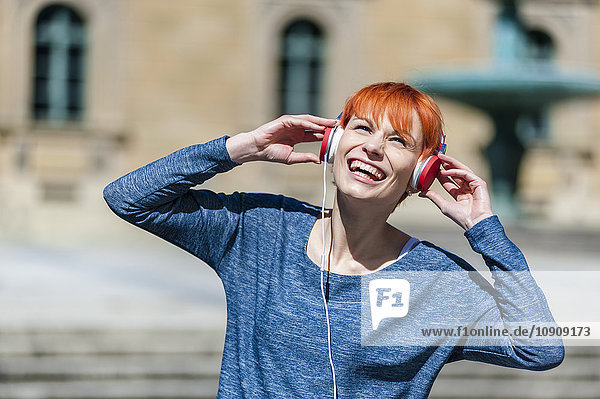 Fröhliche junge Frau beim Musikhören im Freien