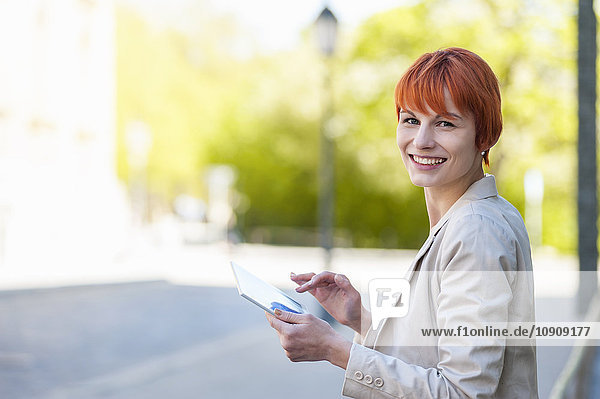 Lächelnde junge Frau im Freien mit digitalem Tablett