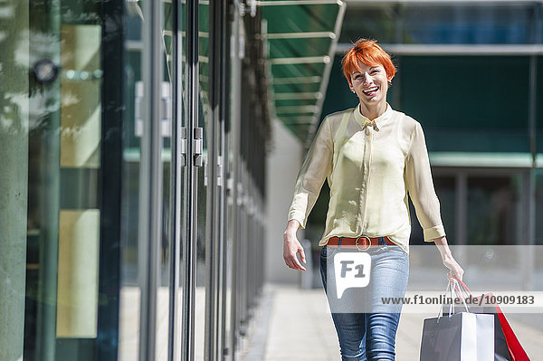 Lächelnde junge Frau mit Einkaufstaschen unterwegs