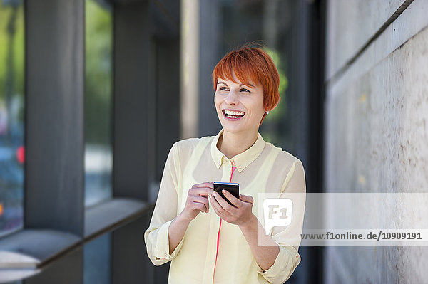 Lächelnde junge Frau im Freien mit Handy