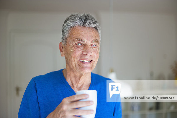 Smiling senior man at home holding cup of coffee