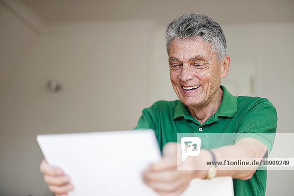 Lächelnder älterer Mann mit digitalem Tablett zu Hause