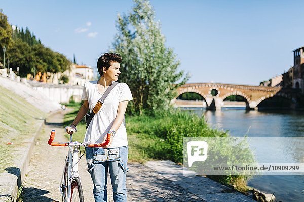 Italien  Verona  junge Frau mit Fahrrad am Flussufer