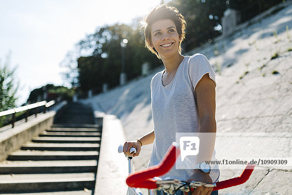 Lächelnde junge Frau mit Fahrrad im Gegenlicht